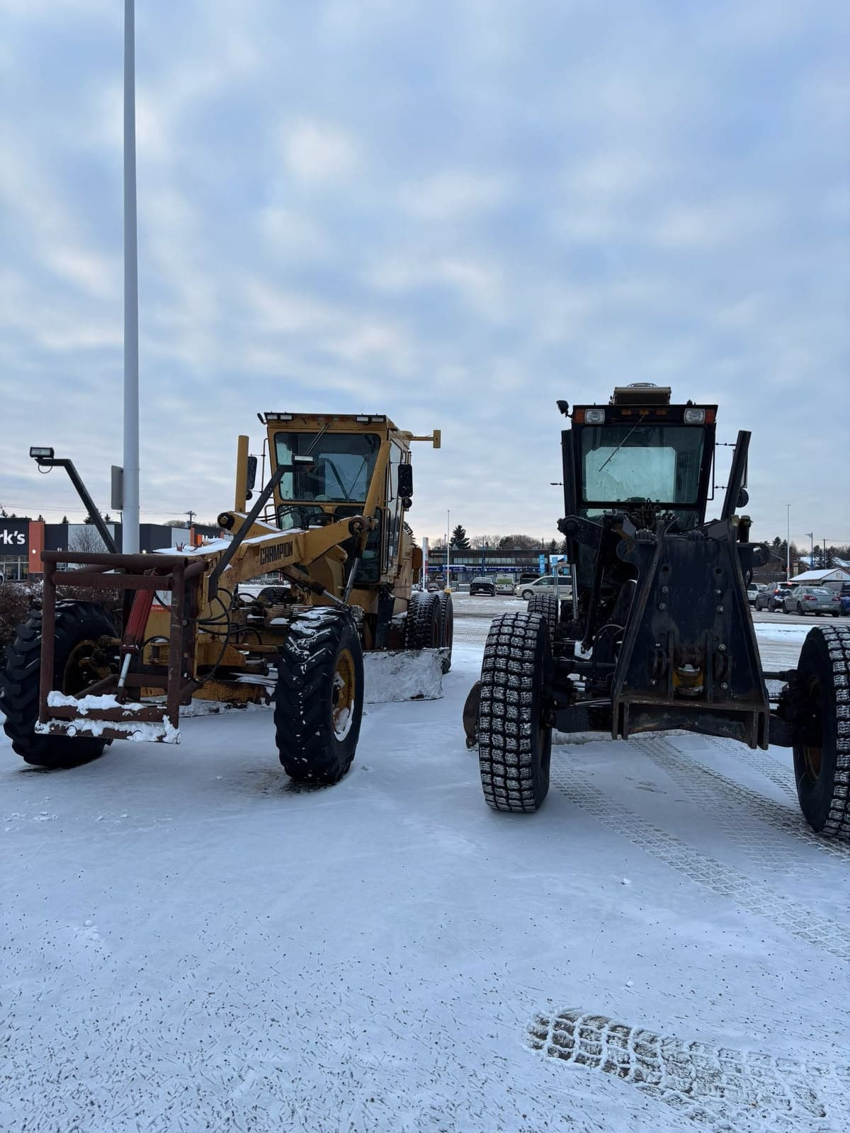 Two road graders parked side by side on a snowy lot